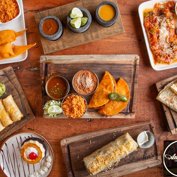 Overhead view of various Mexican dishes, including tacos, burritos, tamales, and dessert, on a wooden table.
