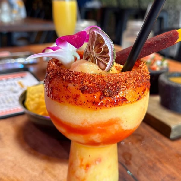 A vibrant Mexican mango margarita with chili-lime rim, dried lime, and orchid garnish.