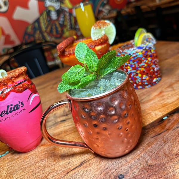 Three colorful Mexican cocktails on a wooden table, including a copper mug with mint.