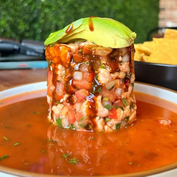 Amelia's Mexican Kitchen's ceviche tower with avocado slices, drizzled sauce, and a side of tortilla chips.