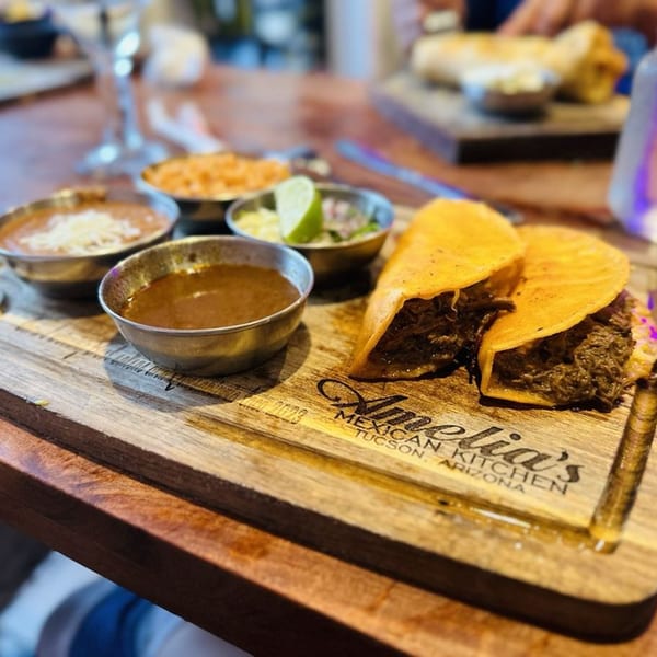 Two beef tacos with sides of rice, beans, and salsa on an Amelia's Mexican Kitchen branded wooden board.