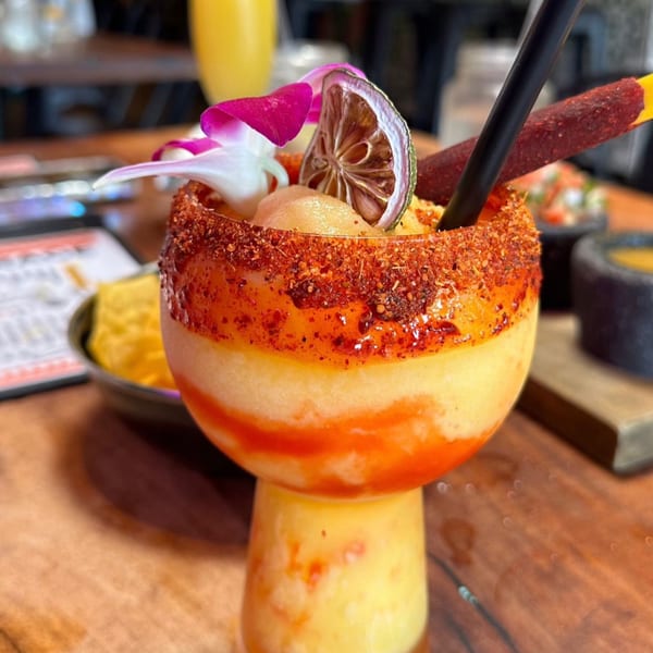 A vibrant mango margarita with a chili-lime rim, garnished with a dried lime and orchid.